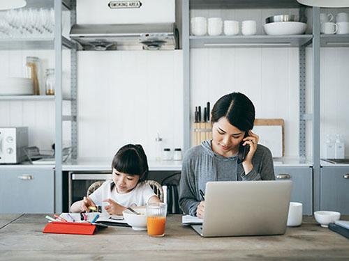 A woman and child sit at a table while she is on a laptop and phone call