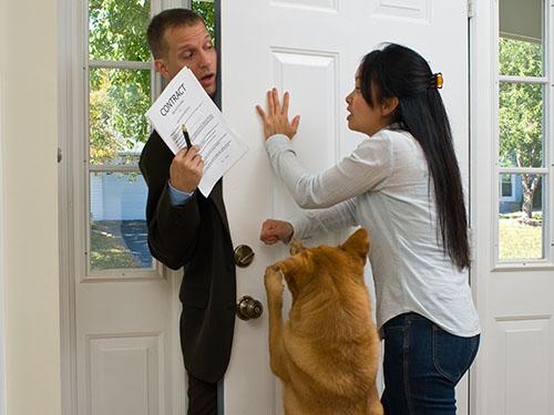 A woman with her dog hold a door shut on a man holding a contract