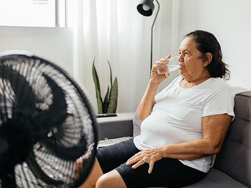 A woman drinks water in front of a fan